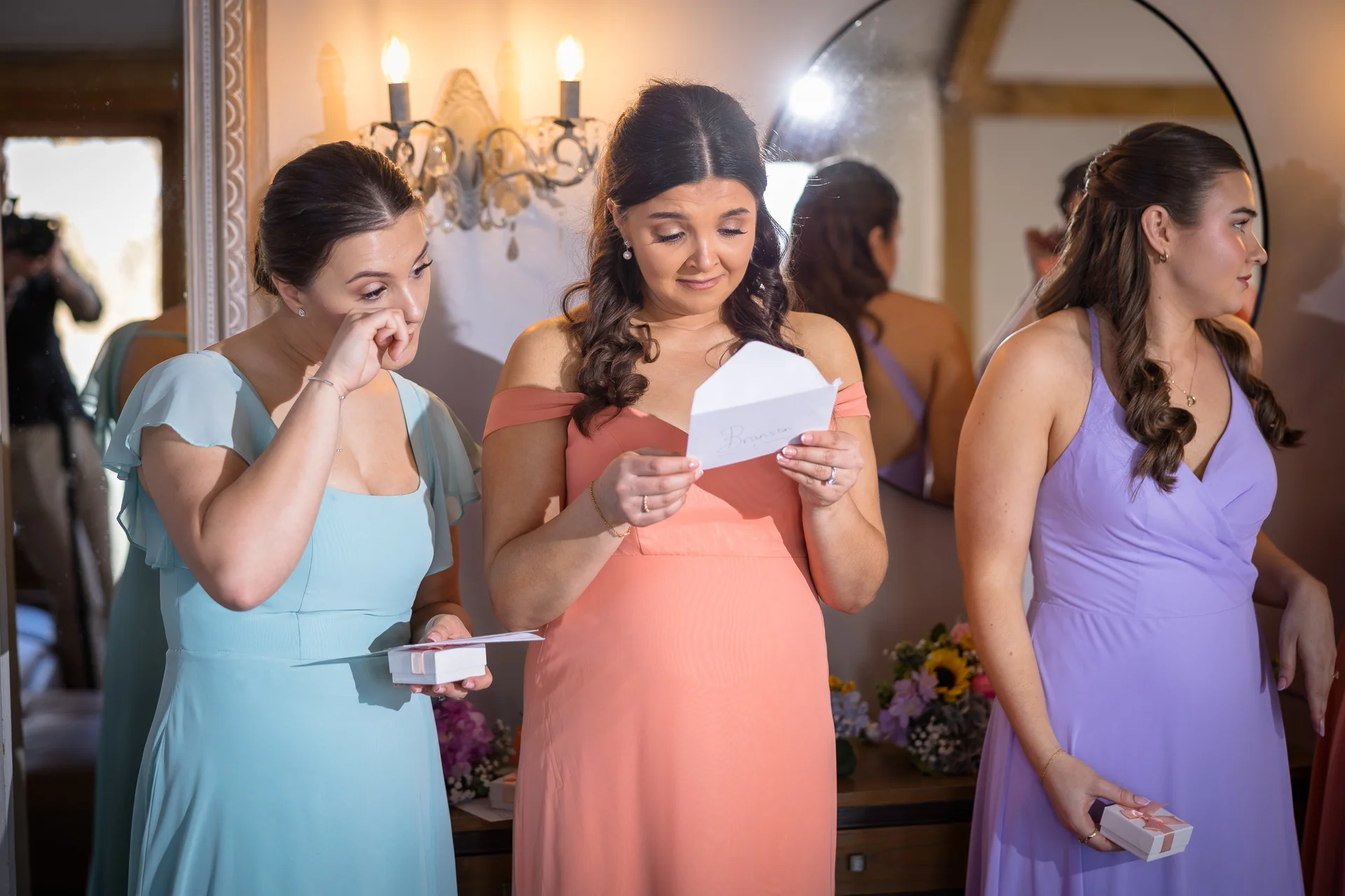 An emotional bride reads a heartfelt letter while standing with her bridesmaids in colourful pastel dresses during morning wedding preparations.
