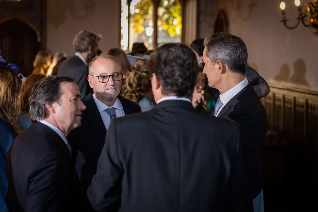 Wedding guests mingle and converse in a warmly lit, wood-panelled reception hall during the drinks reception.