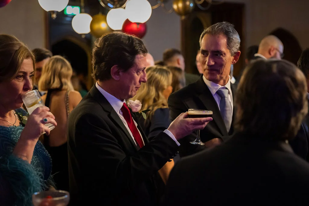 Wedding guests mingle during the evening drinks reception, chatting and holding cocktails in an indoor venue.