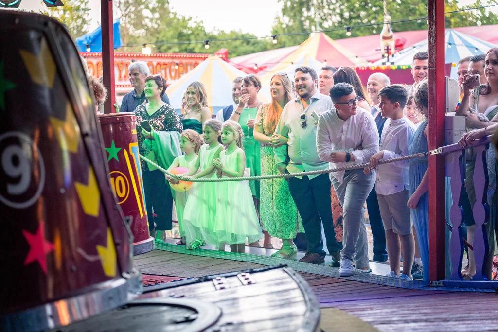 Wedding guests and children smiling and enjoying themselves at a funfair themed wedding celebration.