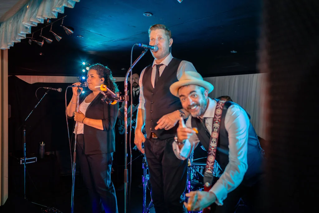 A live wedding band performs on stage under dynamic blue and warm stage lighting during an evening reception.