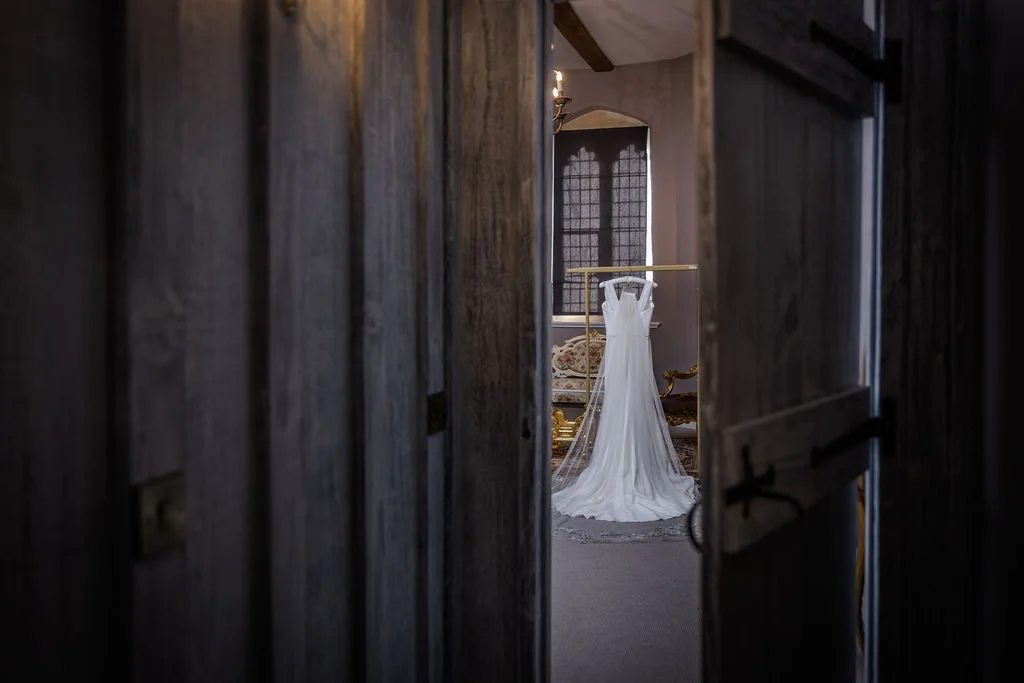 A bridal gown on a rail is viewed through rustic wooden doors during the morning preparations.