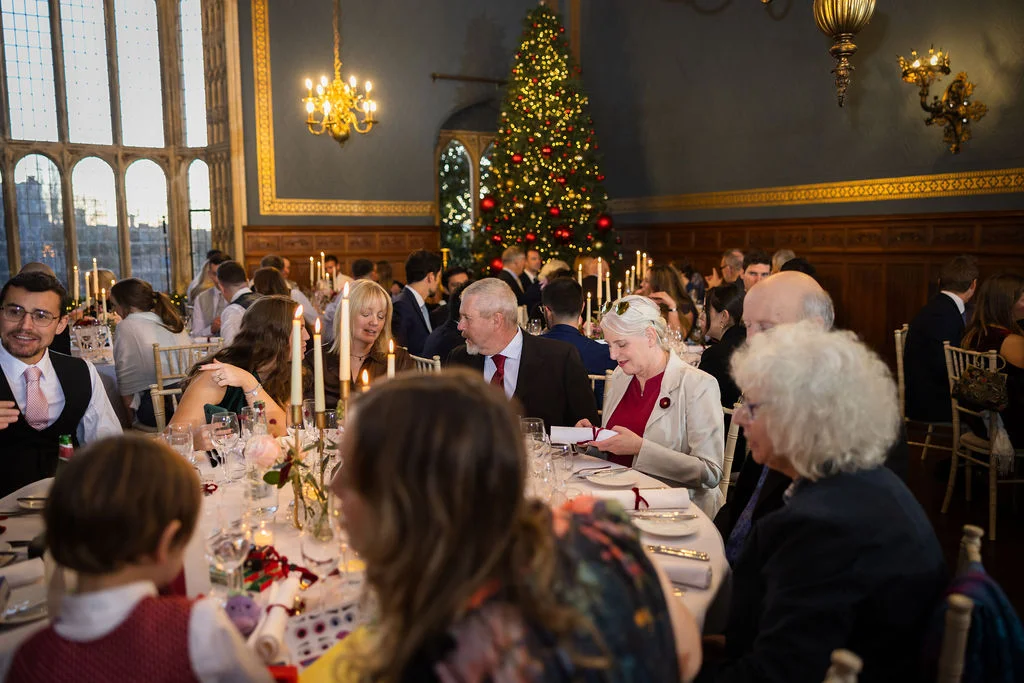 Guests enjoy a festive wedding breakfast inside a grand stately home featuring a large decorated Christmas tree and candlelit tables.