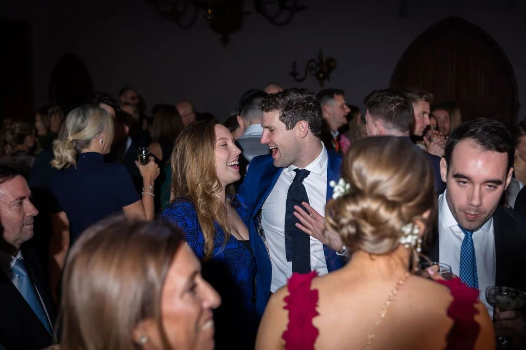 A lively evening wedding reception where guests are mingling and sharing a joyful laugh together in a dimly lit room.