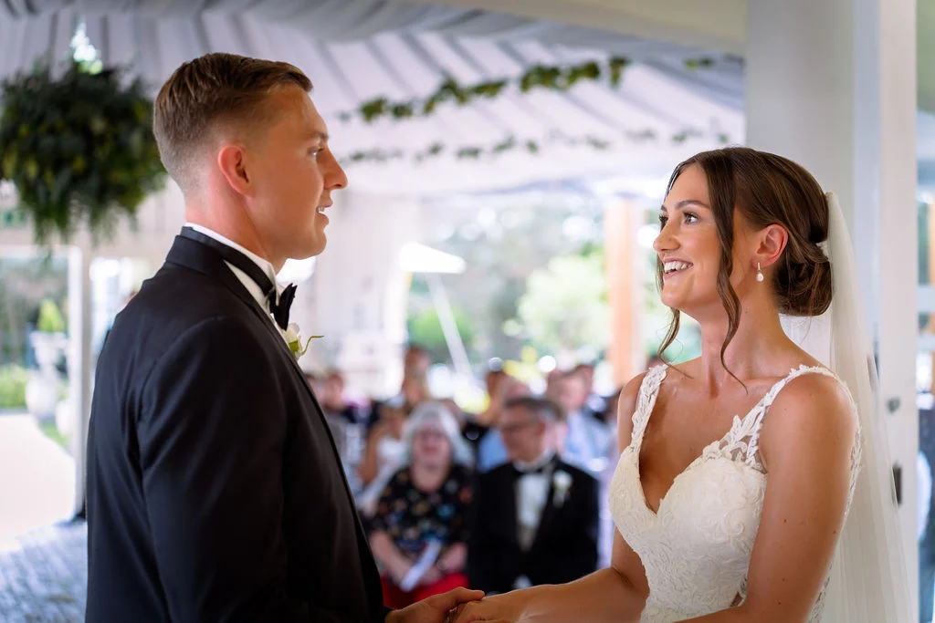 A bride and groom smiling at each other during their wedding ceremony.