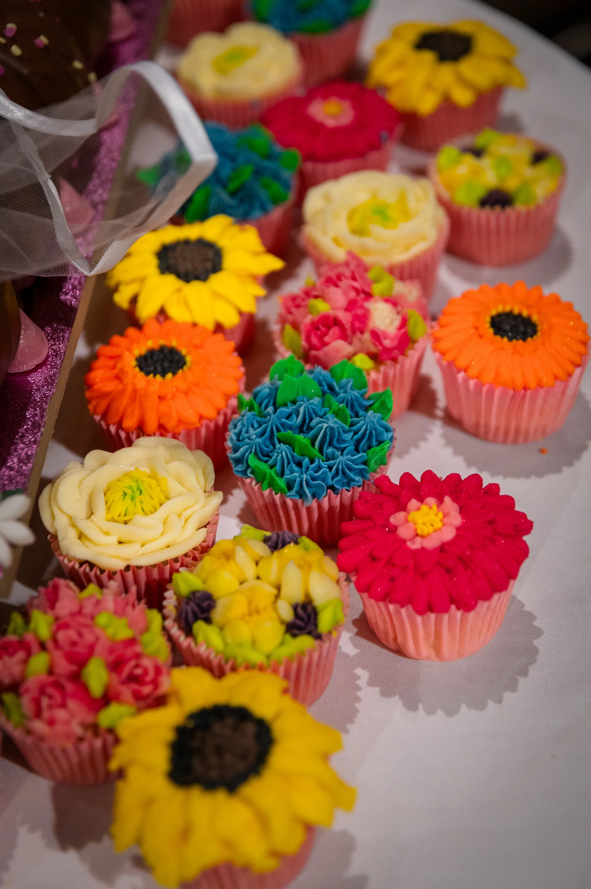 A vibrant assortment of beautifully decorated wedding cupcakes featuring intricate floral icing designs in bright yellow, pink, orange, and blue.