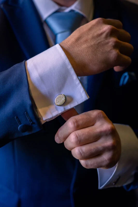 A close-up shot of a groom in a navy suit meticulously adjusting his cufflinks and French cuffs on his wedding day morning.