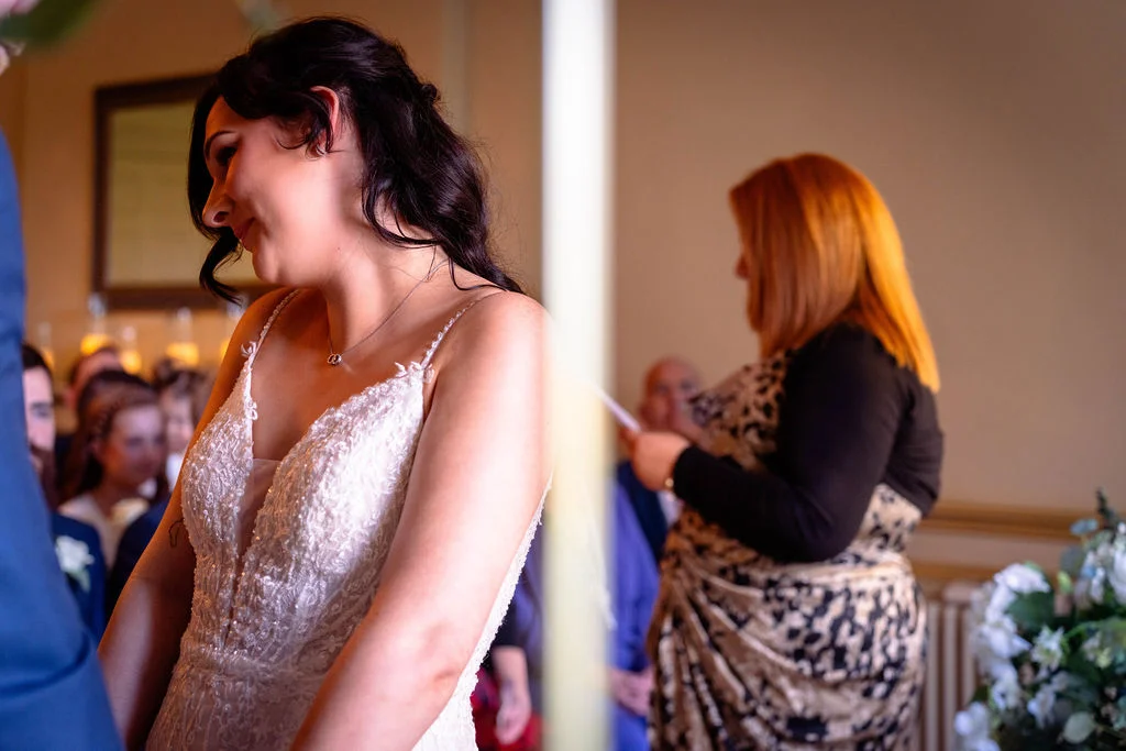 A smiling bride wearing a beaded lace wedding dress with a v neckline during an indoor wedding ceremony.