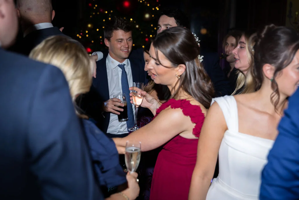 Wedding guests mingle and chat during an evening reception with festive holiday decor in the background.