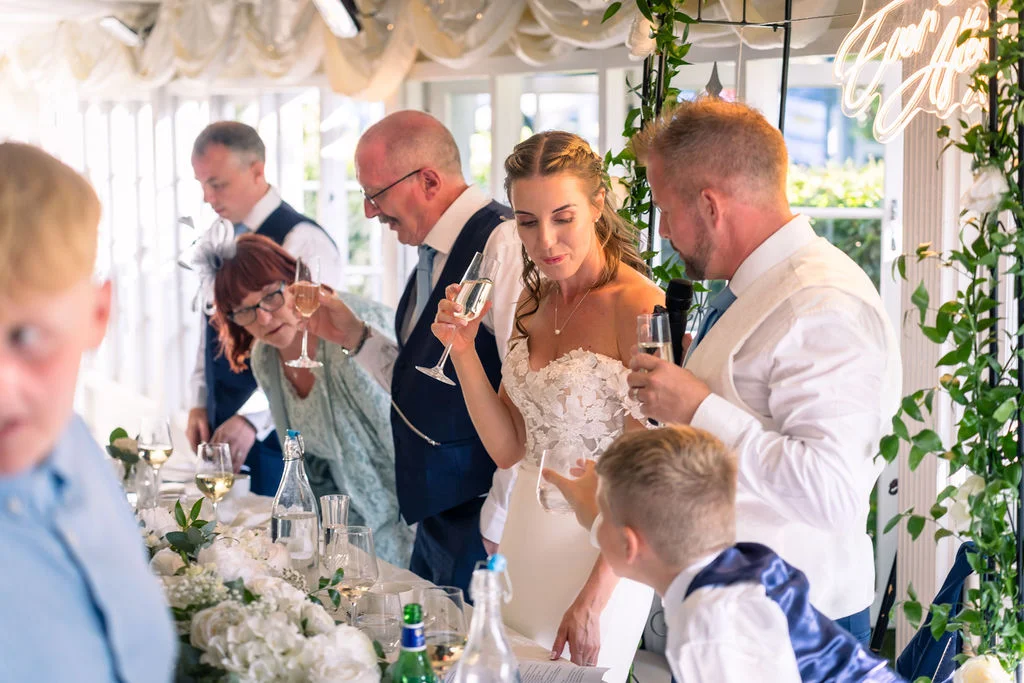 The bride and groom raise their glasses for a toast alongside family members during the wedding speeches at the top table.