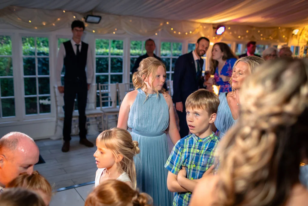 A candid shot of young wedding guests and family members gathered together inside a brightly lit marquee during the evening reception.