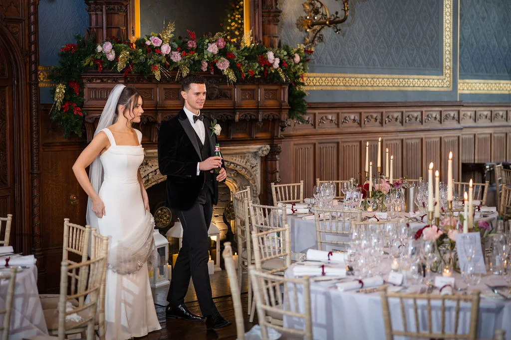 The newly married couple make their grand entrance into a wood-panelled castle reception room decorated with festive mantelpiece florals and candlelit tables.