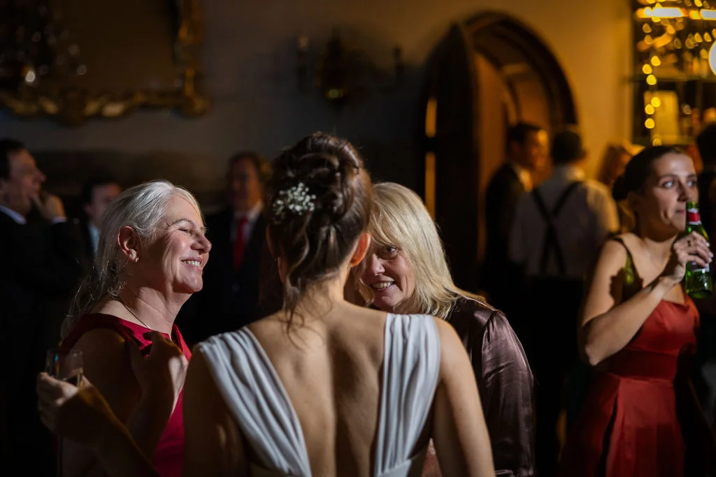 Wedding guests smiling and mingling indoors during an evening reception, illuminated by warm, ambient lighting.