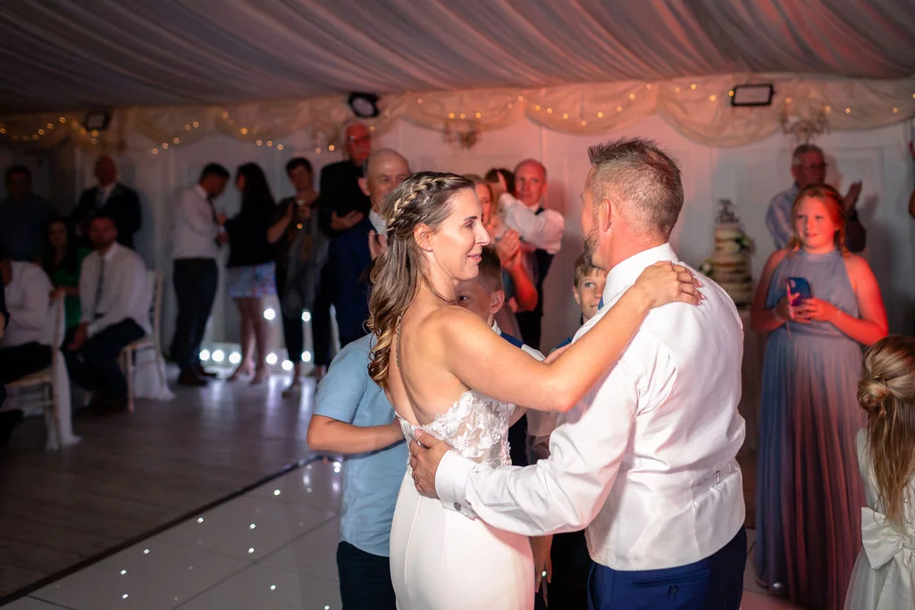 The newly married couple share their first dance on a starlit dance floor inside a marquee surrounded by watching guests.