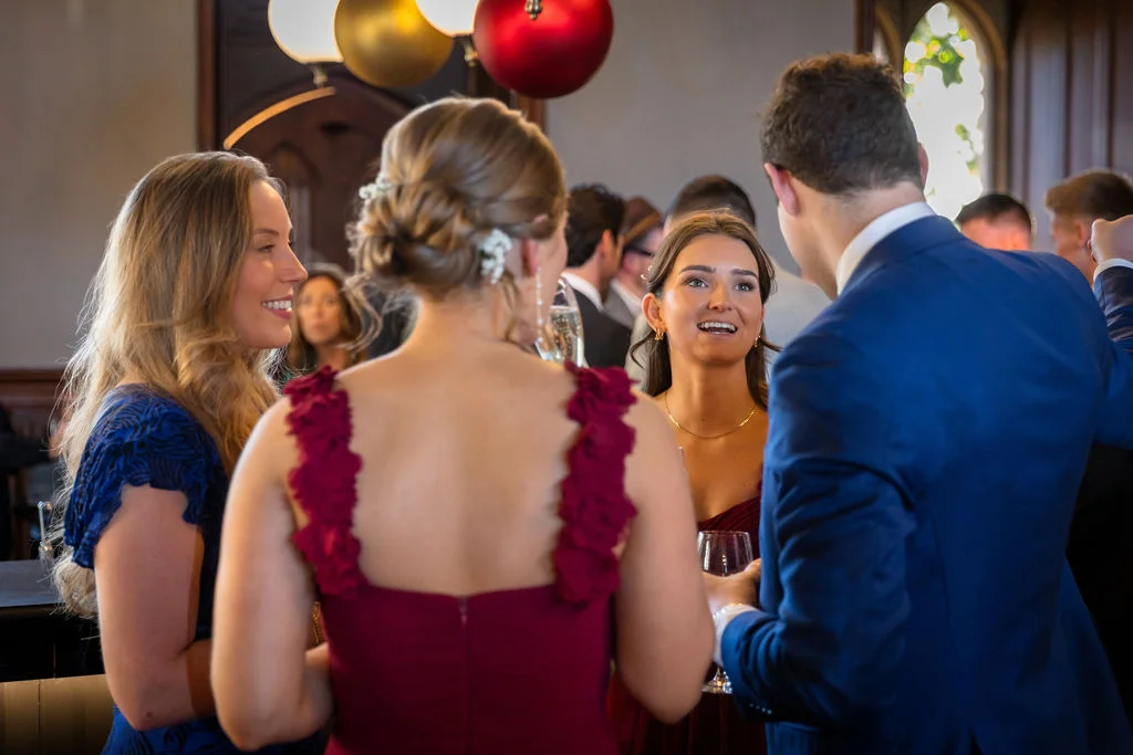 A group of wedding guests mingle and chat happily during the drinks reception inside an elegant venue.