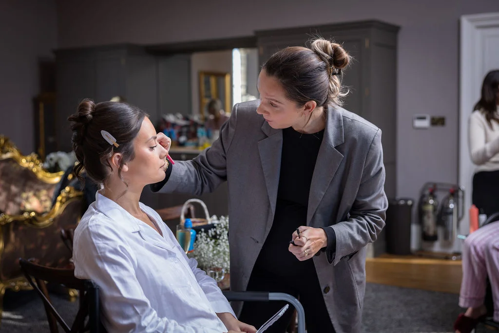 A bride having her makeup carefully applied by a makeup artist during the morning wedding preparations.