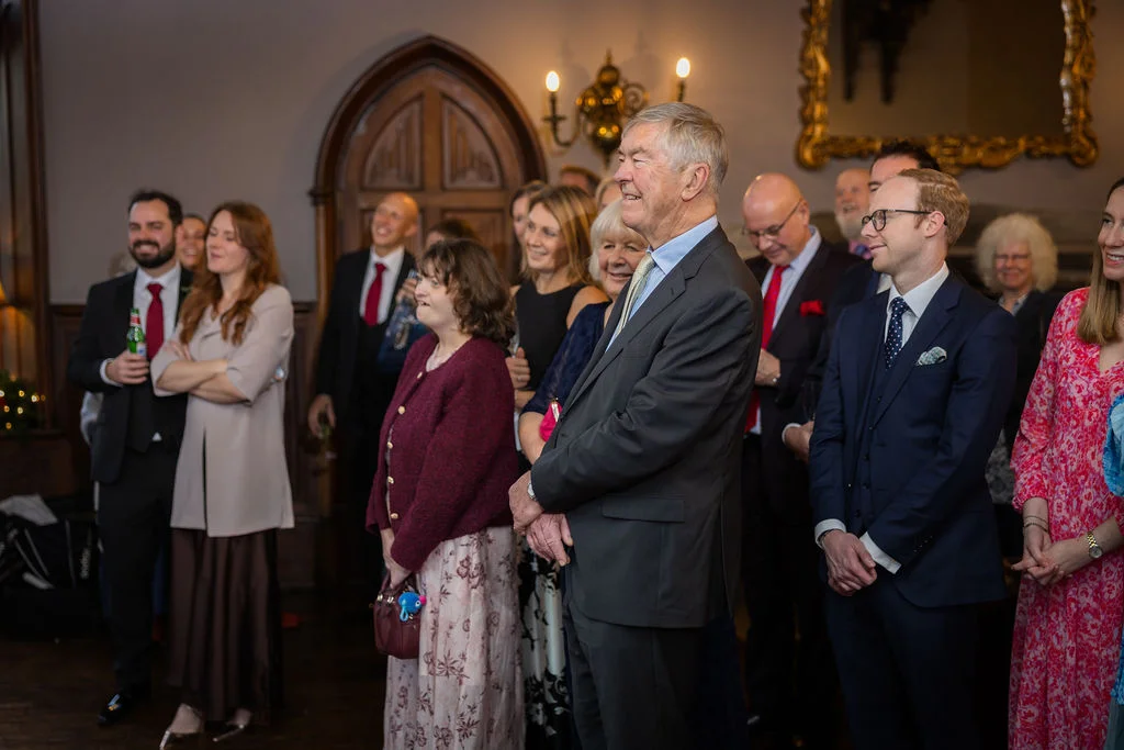 A gathered group of wedding guests smiling and watching happily during the wedding reception speeches.