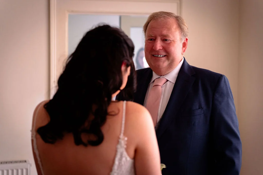 A proud father smiles warmly as he shares a special first look moment with his bride daughter during wedding preparations.