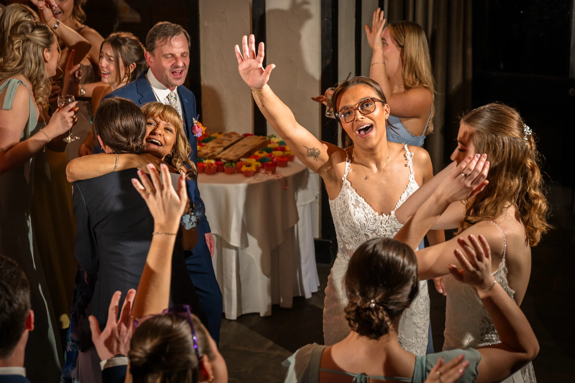 A joyful group of wedding guests and a smiling bride celebrate energetically on the dance floor during the evening reception.