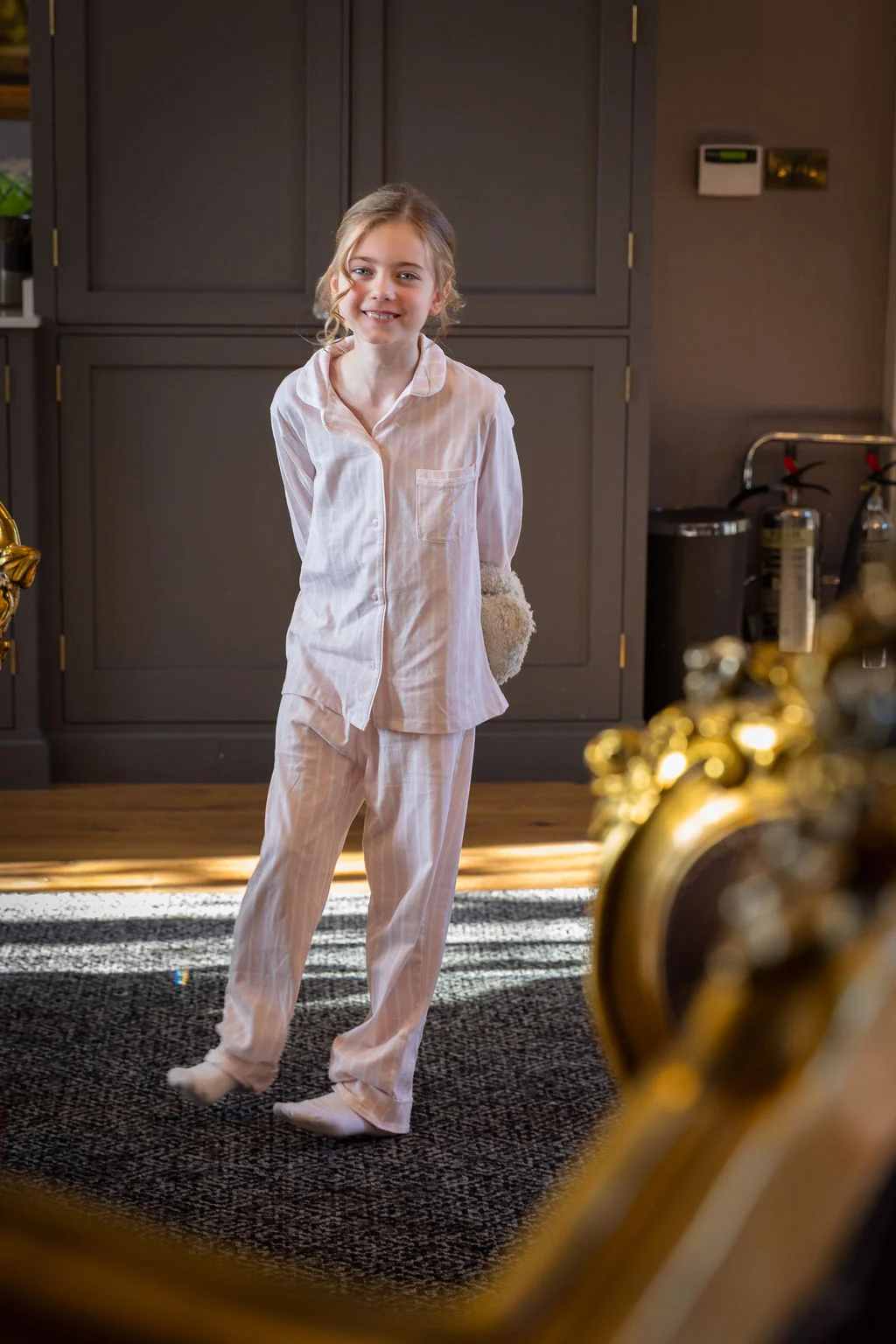 A young flower girl smiles happily while wearing matching striped pyjamas indoors during morning bridal preparations.