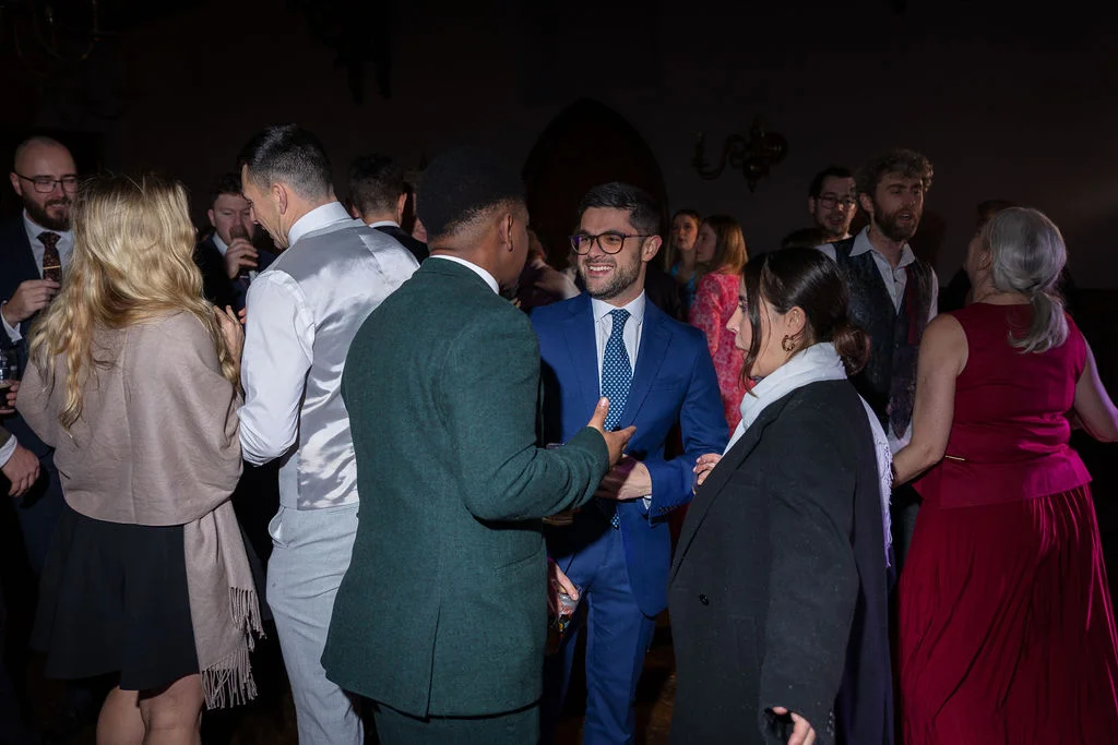 A group of wedding guests mingle and chat together during the lively evening reception inside a dimly lit venue.