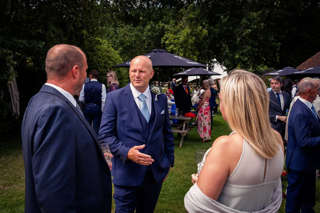 Wedding guests mingling and chatting in a lush outdoor garden setting during a summer drinks reception.