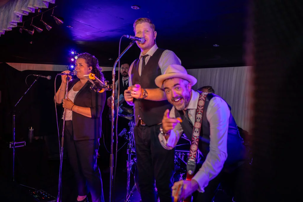 A lively wedding band performs on stage under dramatic blue and purple stage lighting during the evening reception.