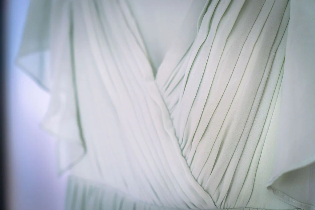Close-up shot of a sage green chiffon bridesmaid dress showcasing the pleated crossover bodice and delicate flutter sleeves.
