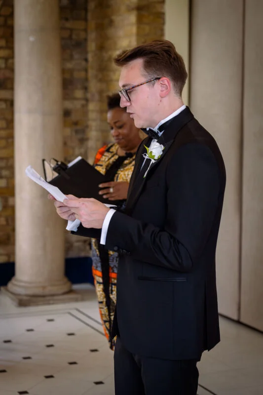 A man in a tuxedo reading a paper.