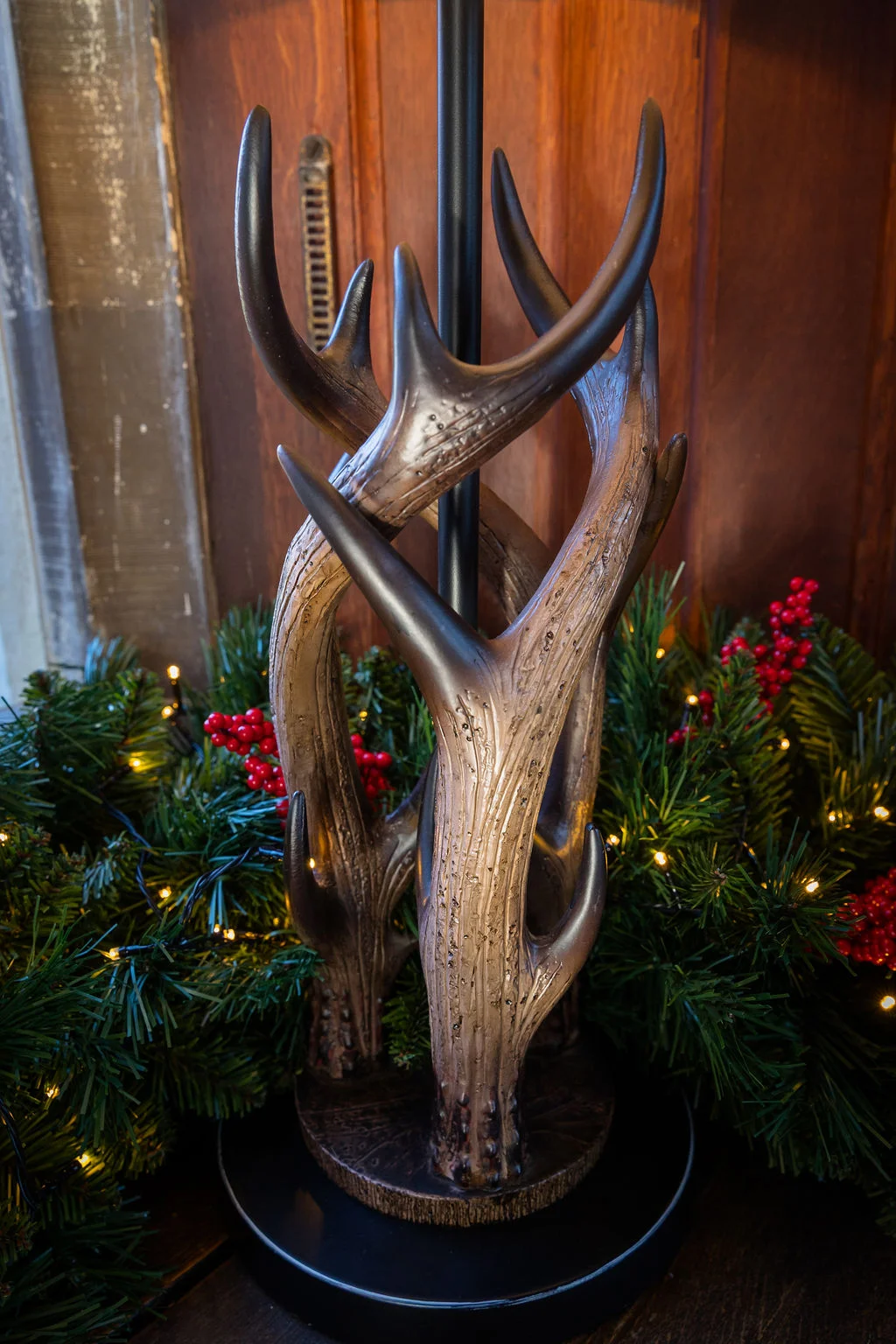 A rustic antler-styled lamp base stands surrounded by a festive green pine wreath with red berries and twinkling fairy lights.