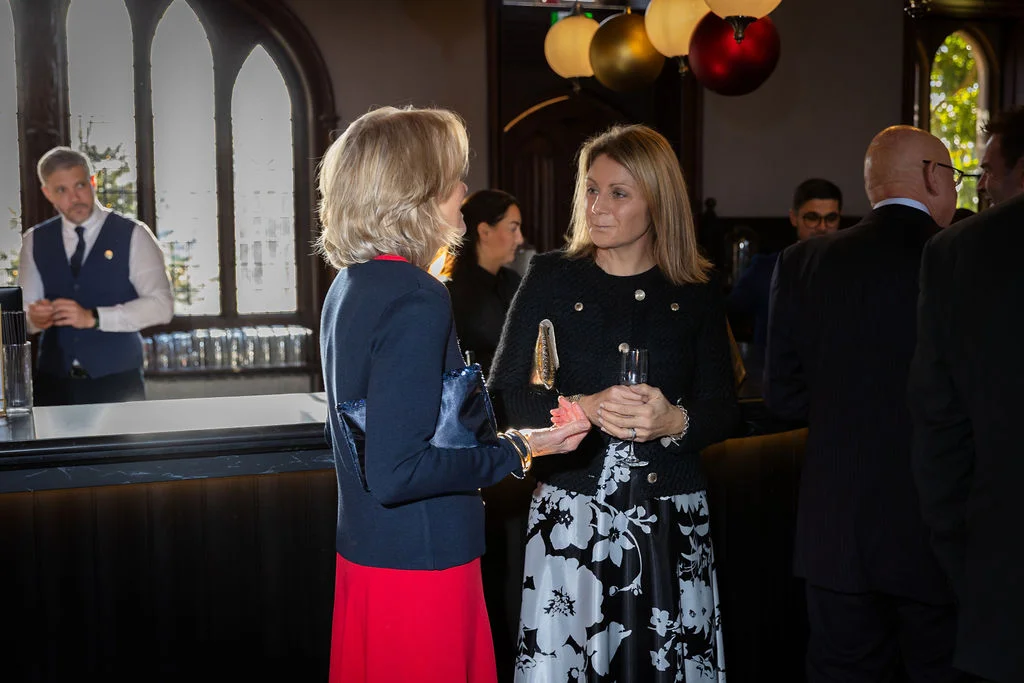Two female wedding guests mingling and chatting near the bar during the drinks reception inside a atmospheric pub venue.