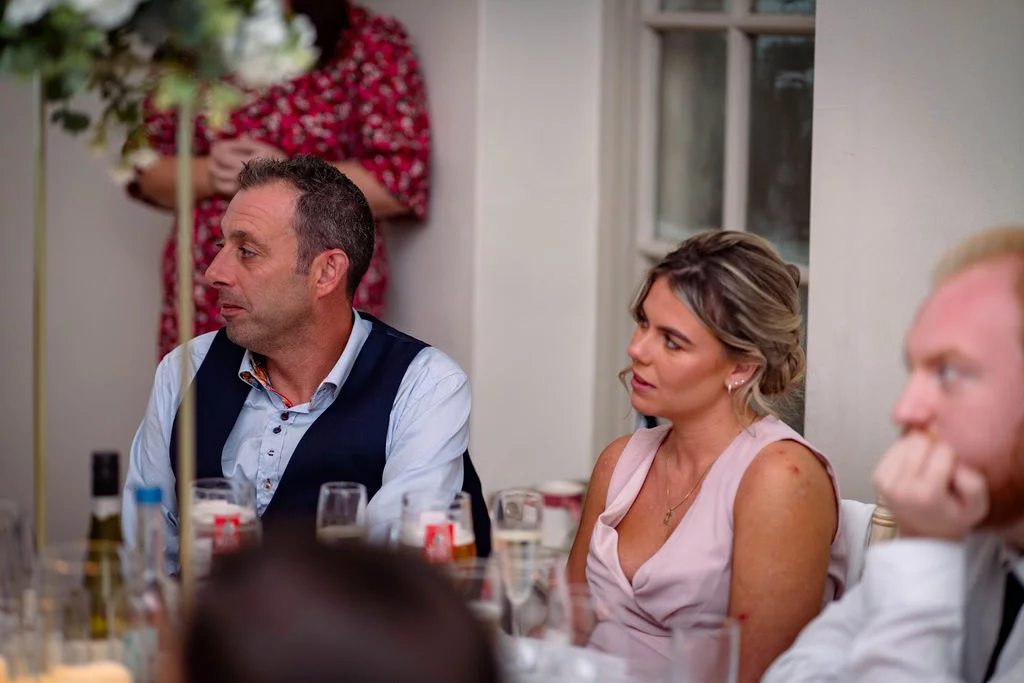 Wedding guests attentively listening and reacting during the wedding breakfast speeches at a reception.