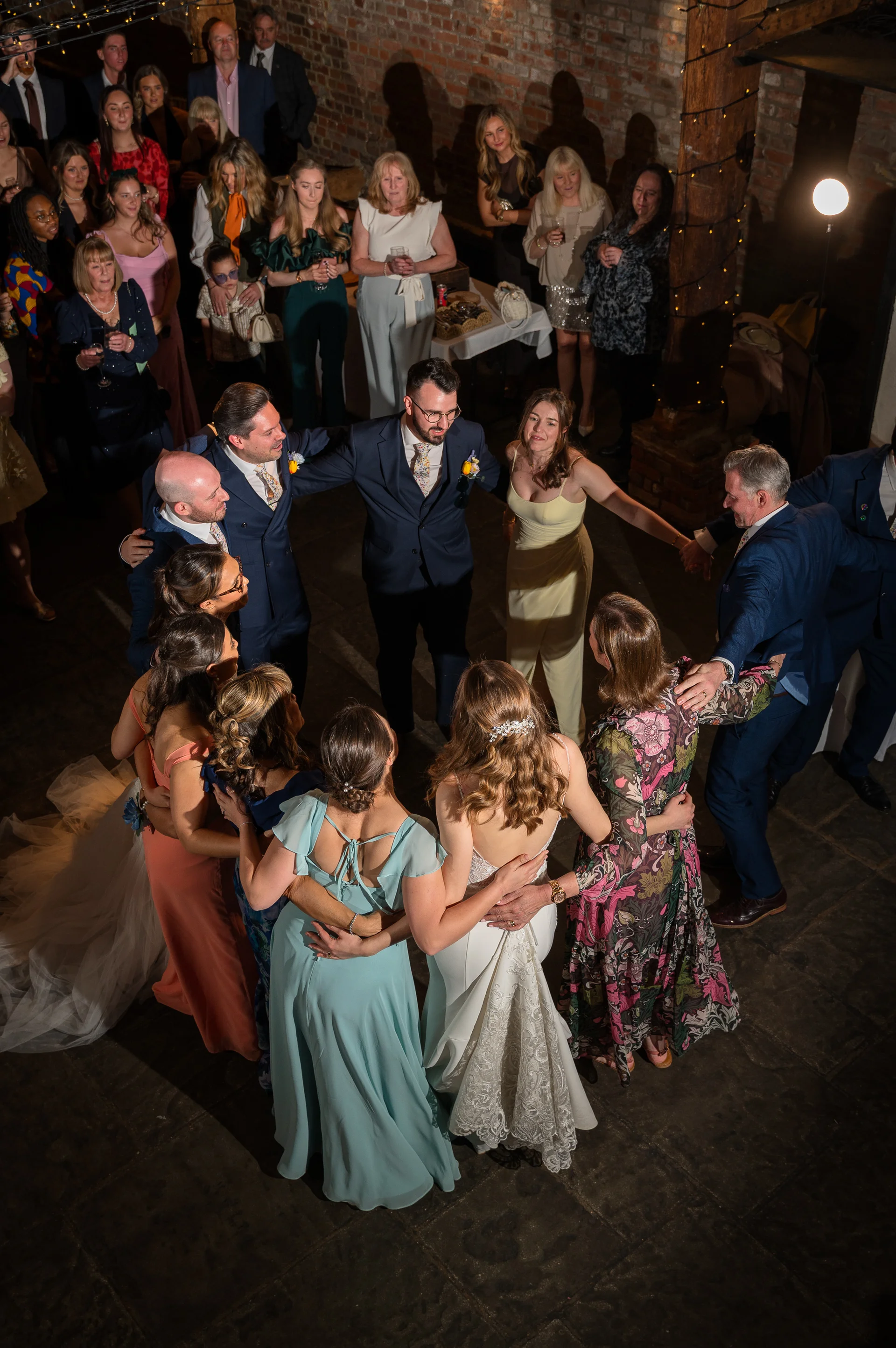 A high-angle shot captures wedding guests and the newly married couple forming a joyous circle on the dance floor of a rustic barn reception.