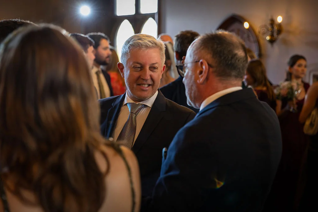 Wedding guests are captured mingling and smiling warmly during a lively indoor reception drinks gathering.