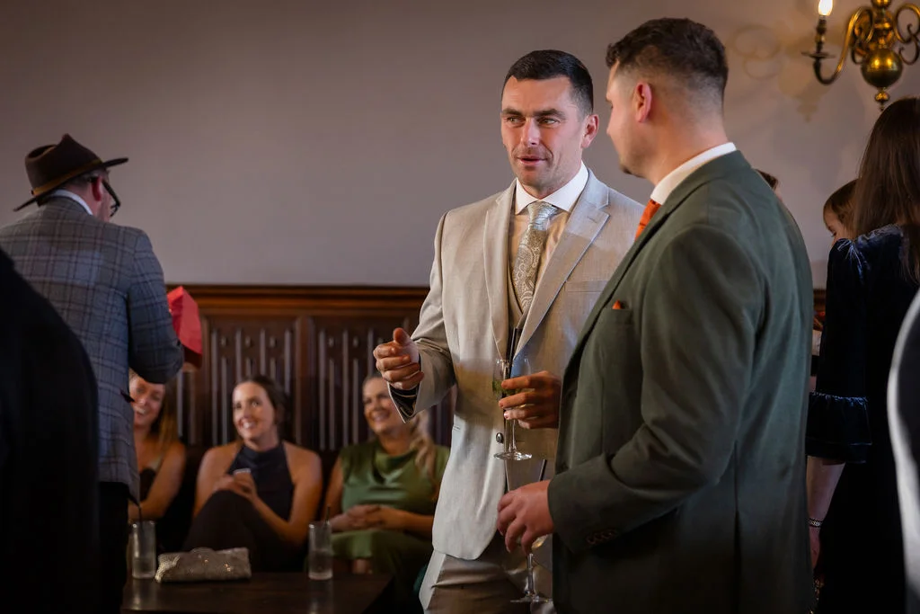 Dressed guests mingle and converse naturally during a wedding drinks reception inside an elegant panelled room.