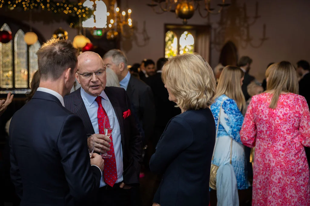 Wedding guests mingle and converse while holding champagne flutes during a lively drinks reception inside an elegant venue.