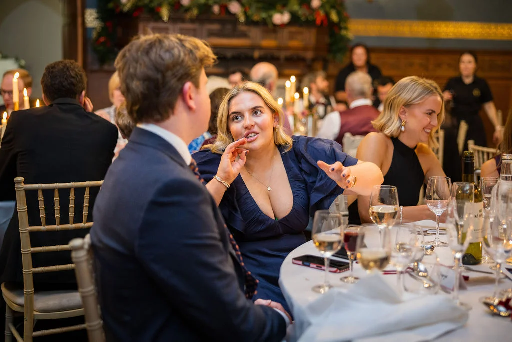 Wedding guests enjoy animated conversation across a round dining table during the evening reception.