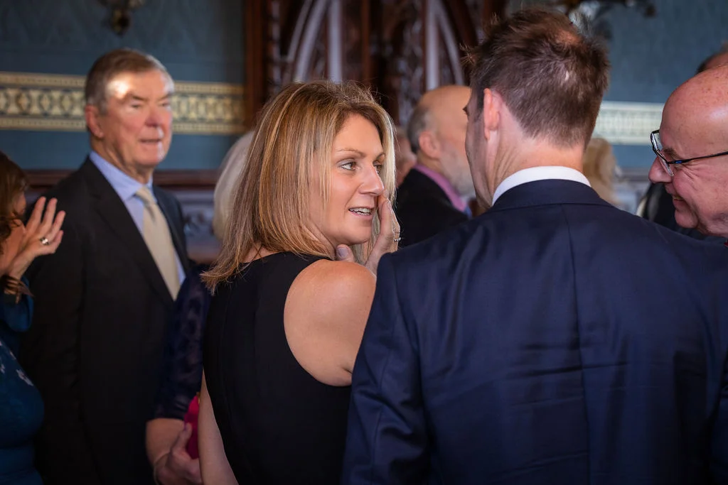Wedding guests mingle and converse candidly indoors during the wedding reception celebration.
