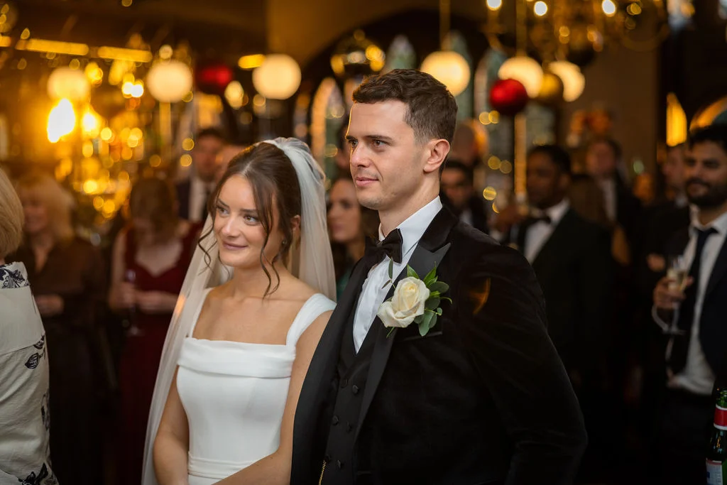 A newly married couple smiling together at an evening wedding reception, with the groom in a black velvet tuxedo and the bride wearing a white gown and veil.