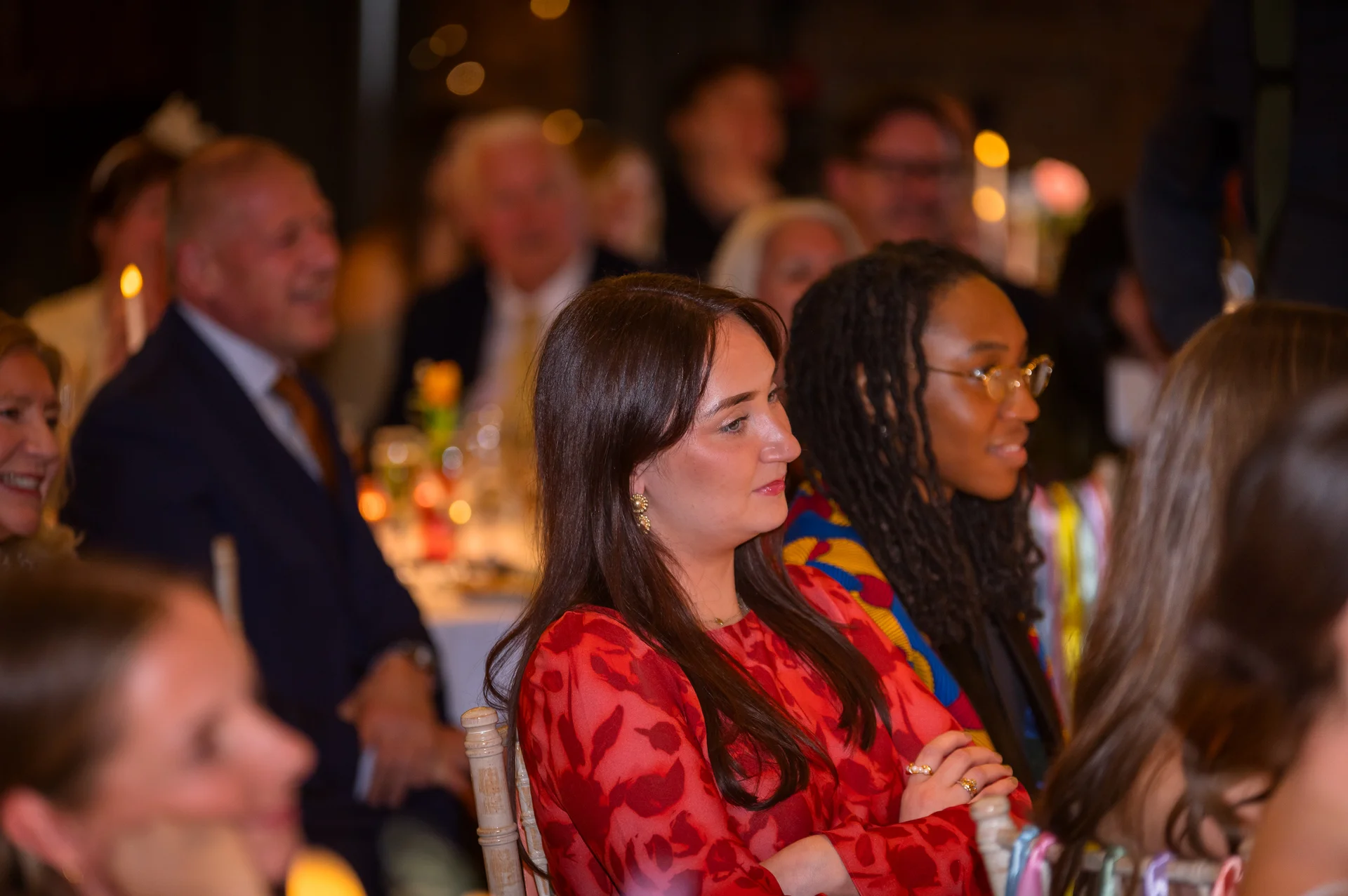 Wedding guests smiling and listening attentively during speeches at an evening reception.