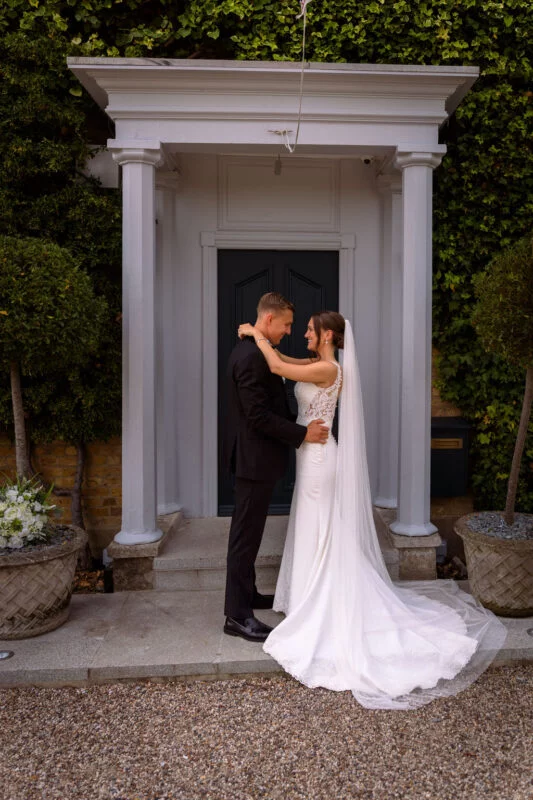 A bride and groom embracing in front of a door.