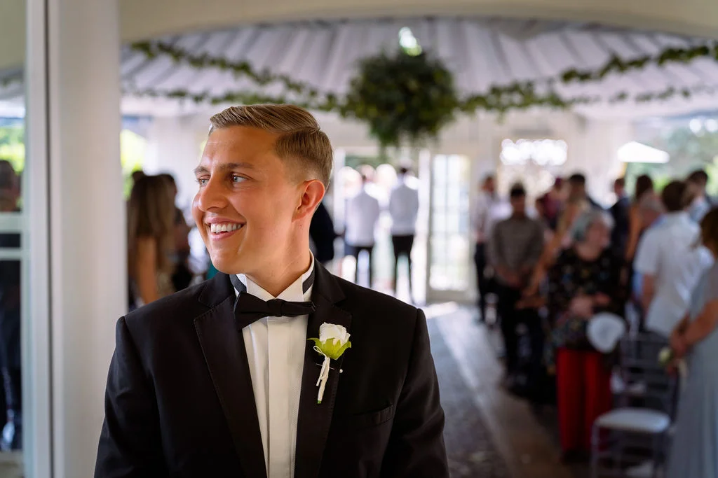 A man in a tuxedo smiles as he walks down the aisle.