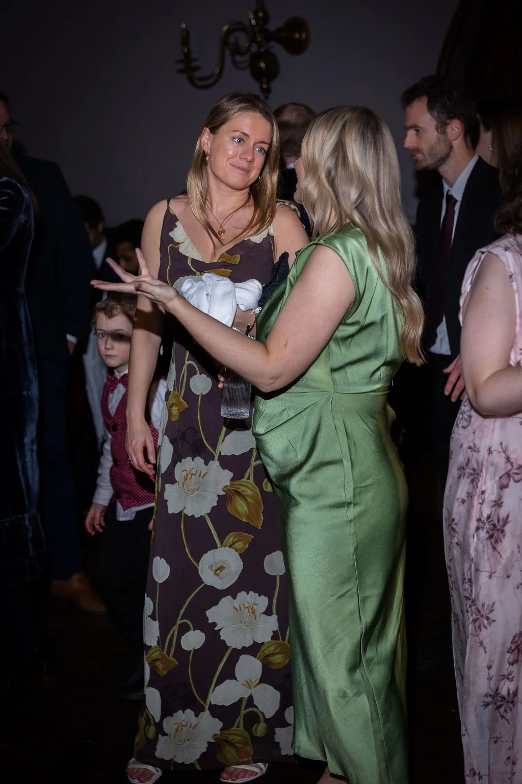 Wedding guests mingling and chatting animatedly during an evening reception in a dimly lit venue.