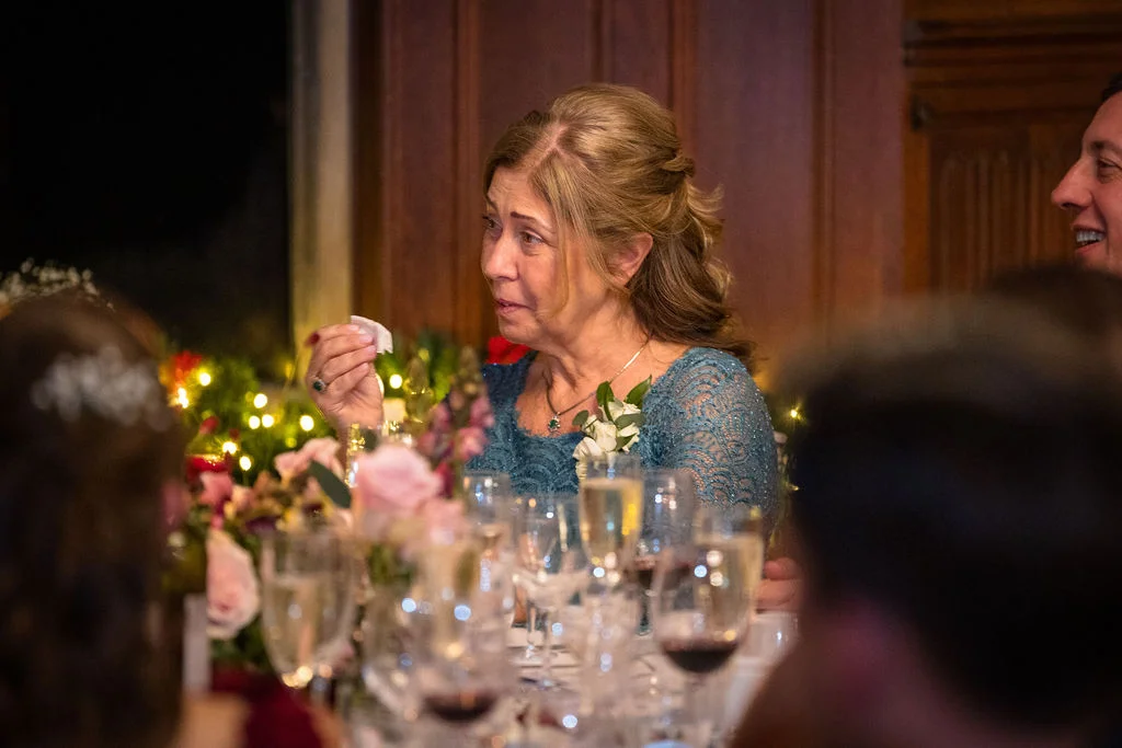 An emotional mother of the bride wipes away a tear with a tissue during the wedding speeches at a candlelit reception.