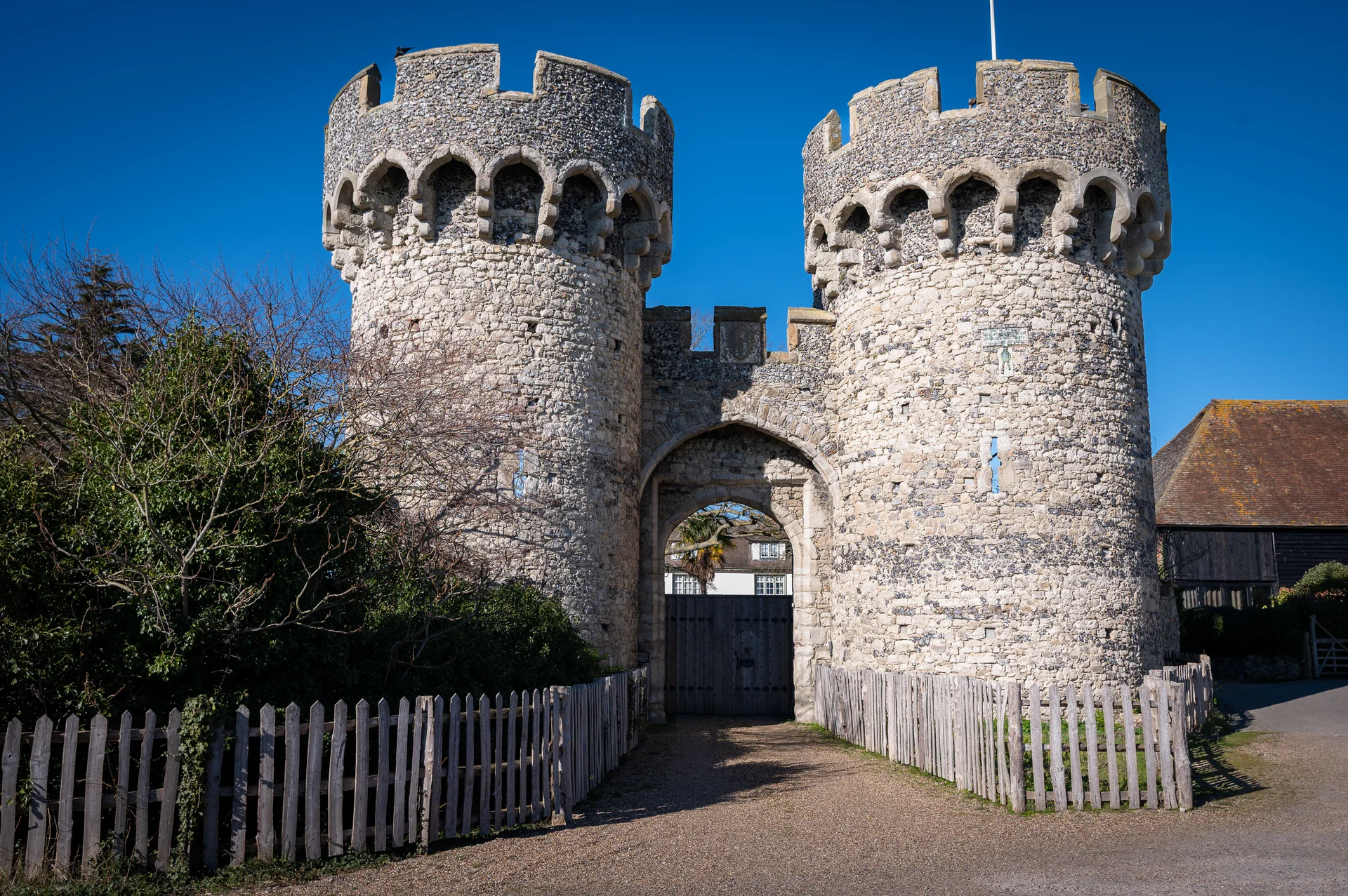 A magnificent historic castle gateway with twin stone towers stands proudly under a clear blue sky on a bright sunny day.