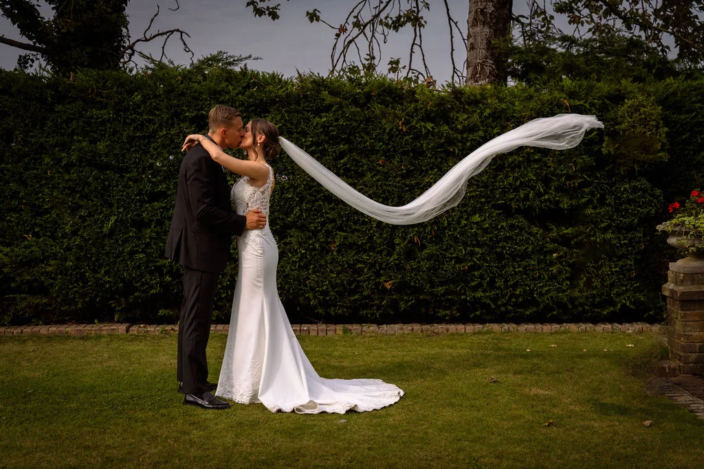 A bride and groom kissing in front of a hedge.