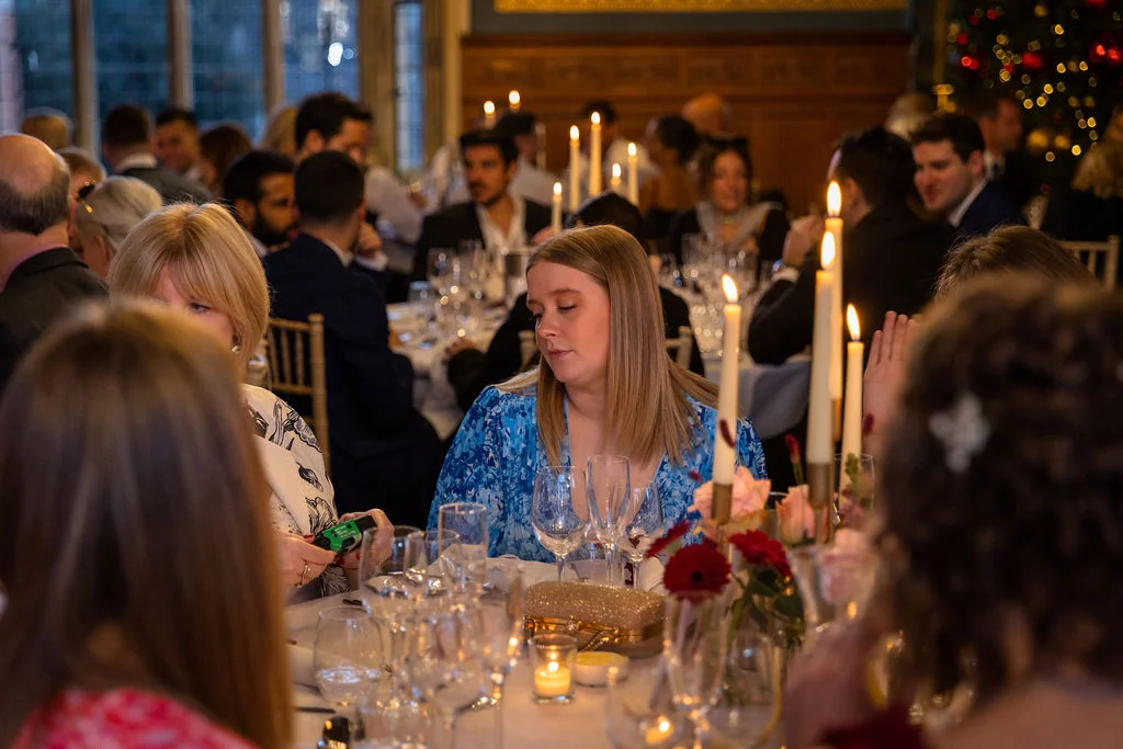 Wedding guests enjoy a candlelit wedding breakfast seated at round tables decorated with floral centrepieces and glowing taper candles.