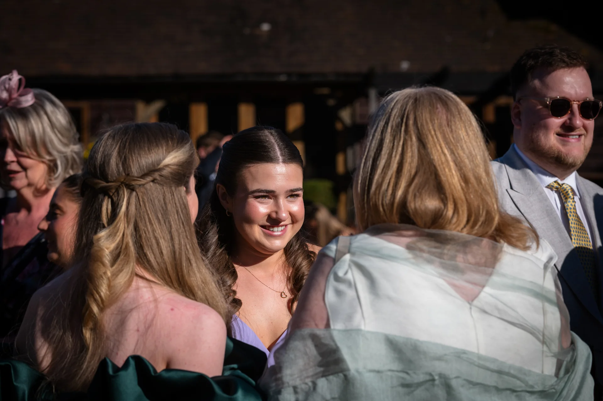 A group of wedding guests enjoying a conversation outdoors in bright sunlight during the drinks reception.