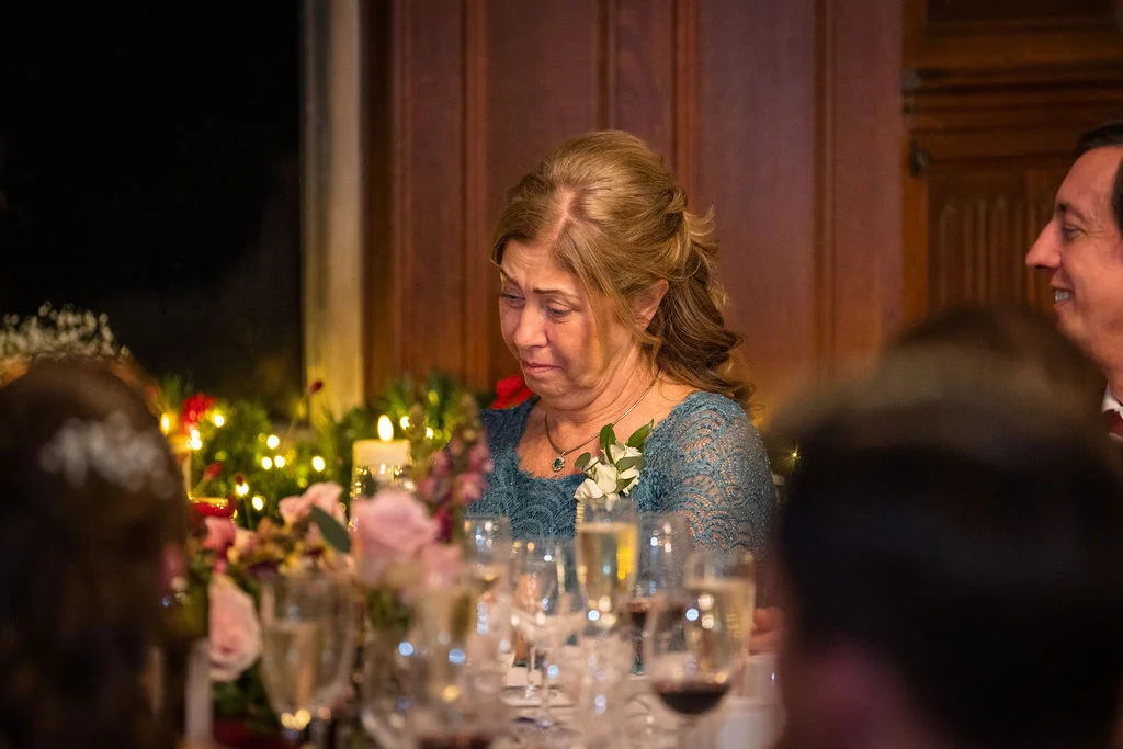 A tearful mother of the bride listens to emotional wedding speeches while seated at a beautifully decorated reception table.