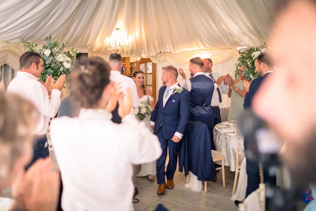 The newlywed couple enters a draped marquee reception to a standing ovation and cheering guests.